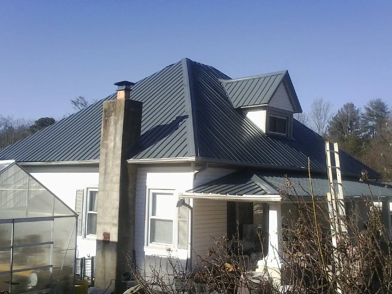 Dark blue standing seam metal roof on a white farmhouse with dormer — Slate & Tile Roof Repair by Roofing Brothers in Moss