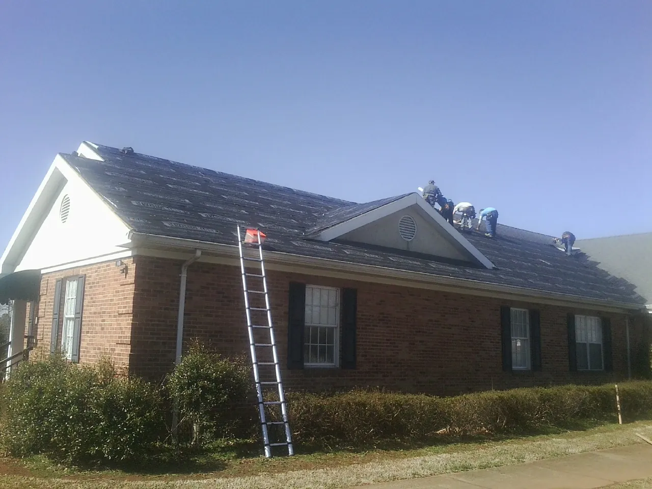 Crew tearing shingles off a brick ranch roof with a ladder set — Metal Roof Repair work by our crew in Moss