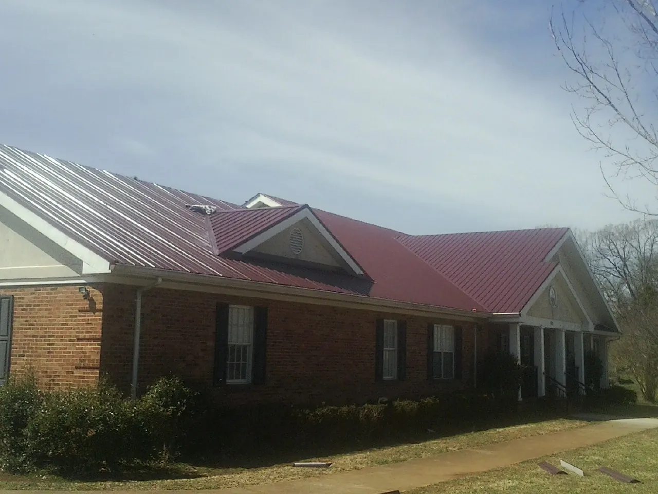 Red metal roof with gabled entries on a long brick building, from a Hail Damage Roof Repair job in Moss