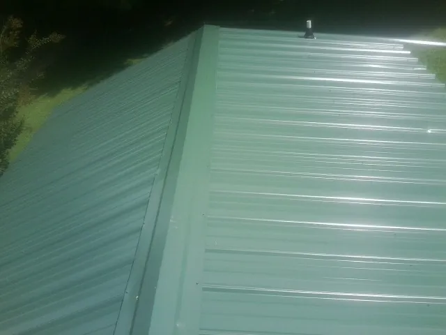 New green metal panels meeting at the ridge of a roof — Flat Roof Repair work by our crew in Moss