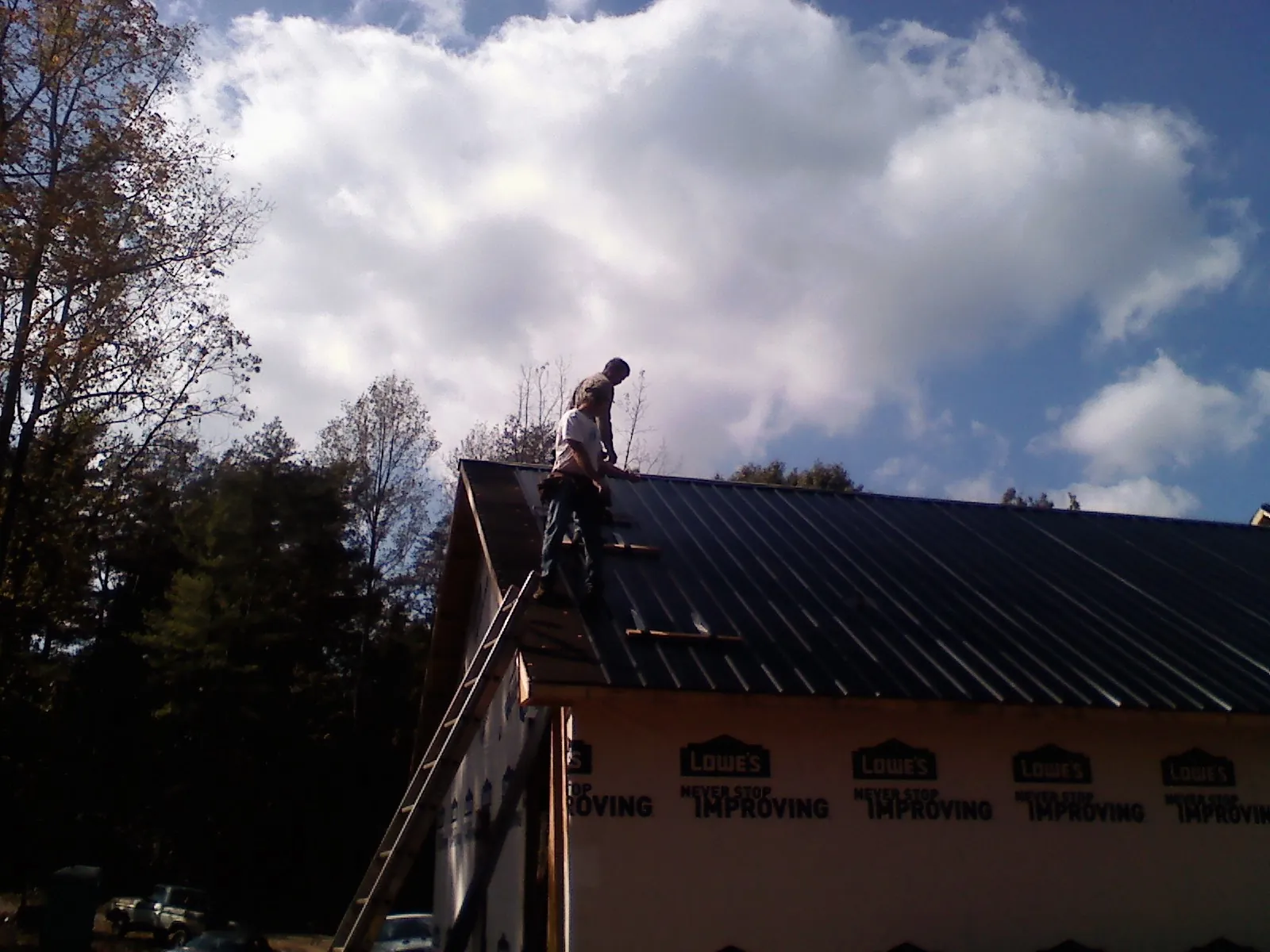 Roofer fastening dark metal panels high against a cloudy sky, from a Roof Inspection job in Moss