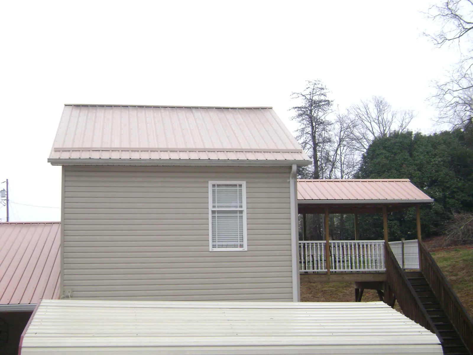Tan metal roofs on a two story addition and attached porch, from a Roof Replacement job in Moss